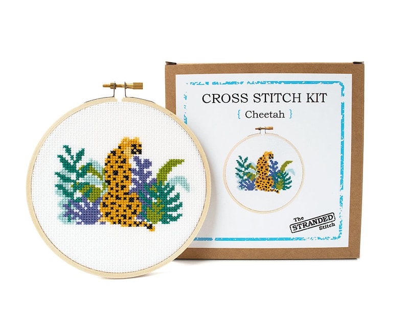 May include: Cross stitch kit featuring a cheetah in a jungle setting. The kit includes a hoop, fabric, floss, and instructions. The box is brown with the text "CROSS STITCH KIT {Cheetah} The STRANDED Stitch"