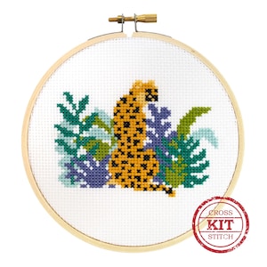 May include: Cross stitch kit featuring a yellow and black leopard sitting in a bed of green and purple leaves. The kit includes all the materials needed to complete the project. The image includes the text "CROSS KIT STITCH".