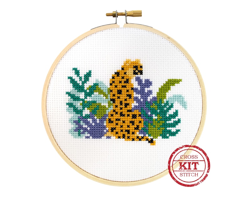 May include: Cross stitch kit featuring a yellow and black leopard sitting in a bed of green and purple leaves. The kit includes all the materials needed to complete the project. The image includes the text "CROSS KIT STITCH".