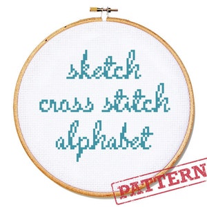 May include: A wooden embroidery hoop holds white fabric with the words "sketch cross stitch alphabet" in teal blue. The word "PATTERN" is stamped in red on the lower right corner. The design is a cross-stitch alphabet.