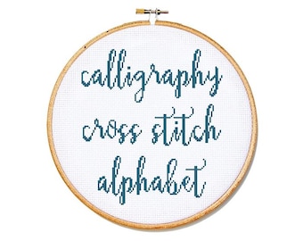 May include: A cross-stitch embroidery hoop with the words "calligraphy cross stitch alphabet" stitched in teal thread on white fabric. The wooden hoop is round and has a brass adjustment screw at the top.