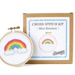 May include: Cross stitch kit with a rainbow and clouds design. The kit includes a hoop, embroidery floss, and instructions. The box is labeled "Cross Stitch Kit {Mini Rainbow} The Stranded Stitch"