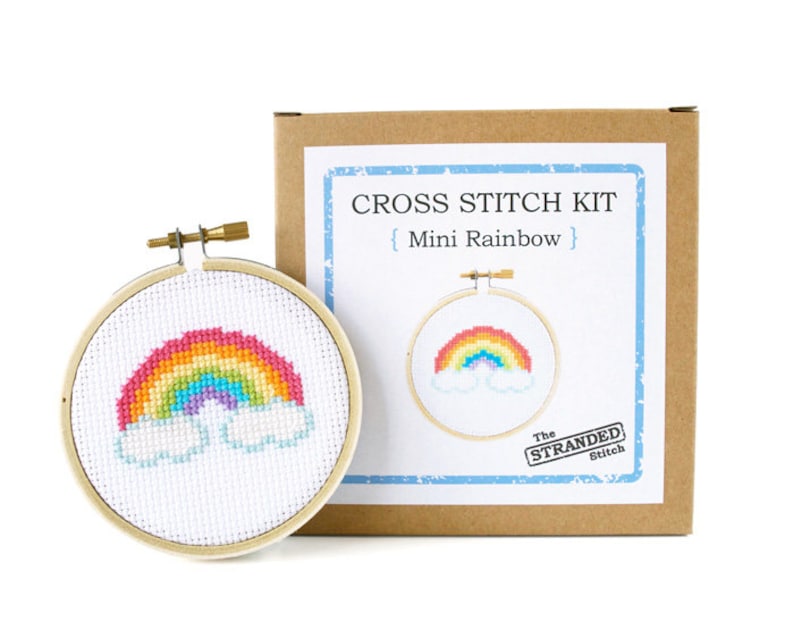 May include: Cross stitch kit with a rainbow and clouds design. The kit includes a hoop, embroidery floss, and instructions. The box is labeled "Cross Stitch Kit {Mini Rainbow} The Stranded Stitch"