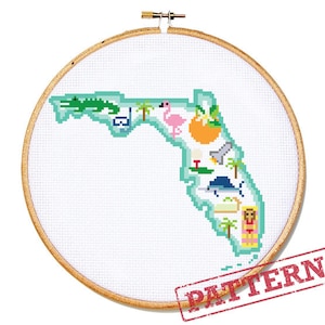 May include: Cross-stitch pattern of the state of Florida, featuring iconic symbols like an alligator, flamingo, and orange. The design is framed in a wooden embroidery hoop. The word "PATTERN" is stamped in red.