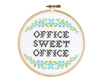 May include: A white embroidery hoop with a wooden frame and a cross-stitch design that reads "Office Sweet Office". The design is surrounded by blue and green flowers.