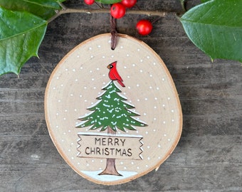 Cardinal atop a snowy pine tree with Merry Christmas sign. Wood burned and painted Christmas ornament. Handmade by Forage Workshop
