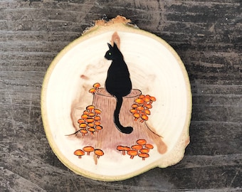 Black cat sitting on a stump with jack o lantern mushrooms on wood slice. Fall ornament or magnet. Handmade by Forage Workshop PREORDER