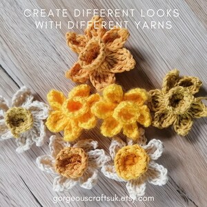 Puede incluir: Seis flores de narciso de ganchillo en diferentes tonos de amarillo y crema. Las flores est&aacute;n dispuestas en forma de tri&aacute;ngulo sobre una superficie de madera. El texto "CREATE DIFFERENT LOOKS WITH DIFFERENT YARNS" est&aacute; en la parte superior de la imagen.