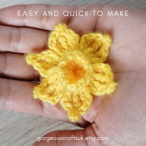 Puede incluir: Una flor de narciso amarilla hecha a crochet con un centro naranja. La flor est&aacute; sostenida en una mano. El texto "EASY AND QUICK TO MAKE" est&aacute; por encima de la flor. El texto "gorgeouscraftsuk.etsy.com" est&aacute; debajo de la flor.