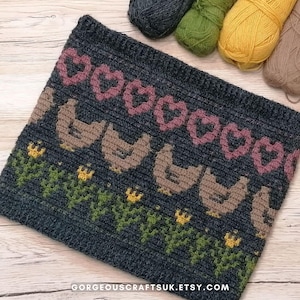 May include: A crocheted grey, brown, pink, green and yellow knitted pattern featuring a row of chickens, flowers and hearts. The pattern is on a grey background and is made with yarn.