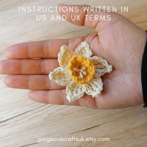 Puede incluir: Una flor de narciso de ganchillo con un centro amarillo y p&eacute;talos blancos. La flor est&aacute; en la mano de una persona.