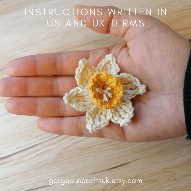Puede incluir: Una flor de narciso de ganchillo con un centro amarillo y p&eacute;talos blancos. La flor est&aacute; en la mano de una persona.