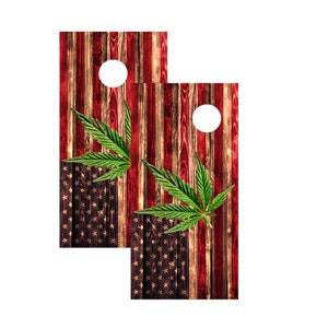 Op de afbeelding: Twee cornhole-borden met een rustiek Amerikaans vlagontwerp. De borden hebben een verweerd houtnerfpatroon met rode en witte strepen en een veld met sterren. Groene cannabisbladeren zijn op de borden geplaatst en elk bord heeft een wit gat.