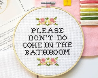 May include: A white embroidery hoop with the text "PLEASE DON'T DO COKE IN THE BATHROOM" in black lettering. The hoop is surrounded by pink and yellow felt and embroidery floss.
