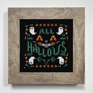 May include: Cross-stitch artwork in a wooden frame. The black background features the words "ALL HALLOWS EVE" in teal, with a cat face and ghost figures. Orange and white accents add to the Halloween theme.