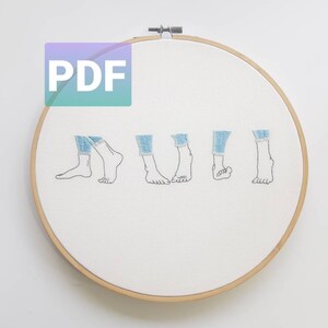 May include: Embroidered design of five pairs of feet in jeans, with the cuffs rolled up, on a white fabric stretched over a wooden embroidery hoop.