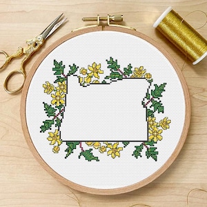 May include: A cross-stitch embroidery hoop with a floral design in yellow and green. The embroidery is set in a wooden hoop, with gold scissors and thread nearby. The design features a rectangular space.