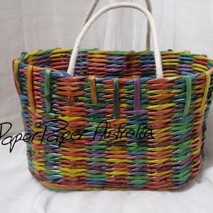 May include: A colorful woven tote bag with a white rope handle. The bag is made from recycled paper and has a rainbow pattern.