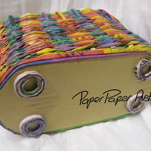 May include: A colorful woven basket with a brown cardboard bottom and rolled paper feet. The basket is made from recycled paper and has the text "Paper Paper Australia" on the bottom.