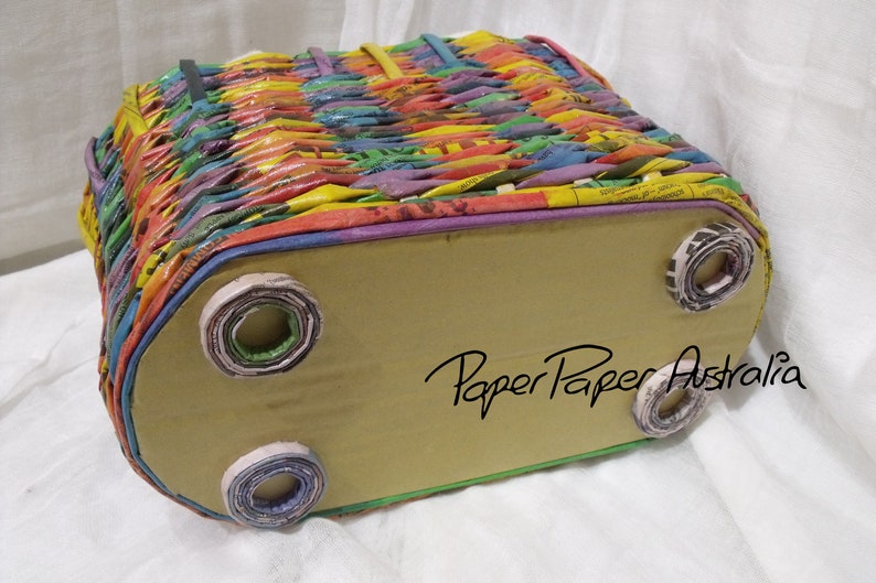 May include: A colorful woven basket with a brown cardboard bottom and rolled paper feet. The basket is made from recycled paper and has the text "Paper Paper Australia" on the bottom.