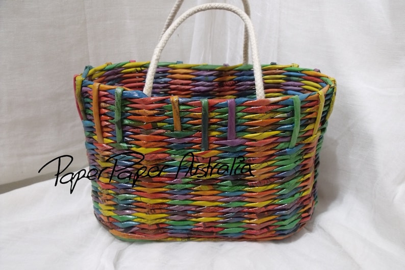 May include: A colorful woven tote bag with a white rope handle. The bag is made from recycled paper and has a rainbow pattern.