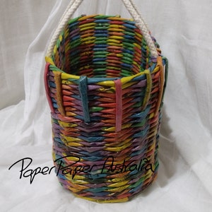 May include: A colorful woven basket with a white rope handle. The basket is made of paper and has a rainbow pattern.