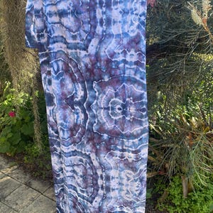 May include: A rectangular fabric scarf featuring a tie-dye pattern with shades of deep navy blue, indigo, and muted purple. The design displays symmetrical, organic, cloud-like shapes with white, vein-like lines throughout the textile surface.