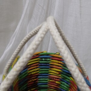 May include: A colorful woven basket with white rope handles. The basket is made from recycled paper and has a rainbow pattern.
