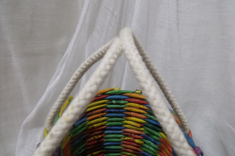 May include: A colorful woven basket with white rope handles. The basket is made from recycled paper and has a rainbow pattern.