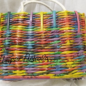 May include: A colorful woven tote bag made from recycled paper. The bag has a white handle and is woven with strips of paper in various colors, including yellow, orange, red, purple, blue, and green. The bag is labeled "Paper Paper Australia".