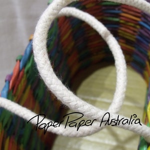 May include: A colorful woven basket with a white rope handle. The basket is made of paper and has a rainbow pattern. The text "Paper Paper Australia" is visible on the basket.