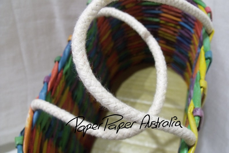May include: A colorful woven basket with a white rope handle. The basket is made of paper and has a rainbow pattern. The text "Paper Paper Australia" is visible on the basket.