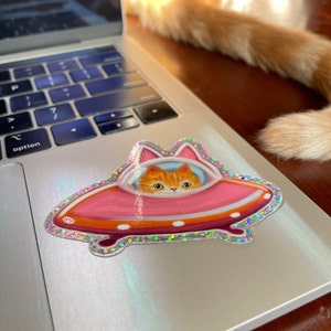 Cute and funny painterly orange kitty cat glitter sticker taking a spin in the abandoned pink alien flying saucer designed just for him-who wouldn’t?