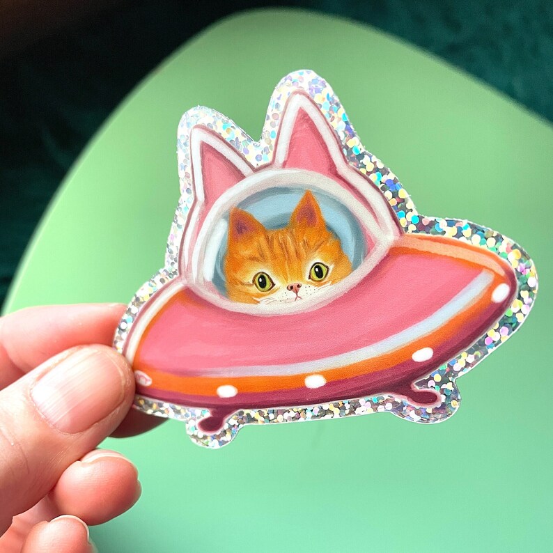 May include: A sparkly pink and orange spaceship sticker with a cute orange cat peeking out of the cockpit window.