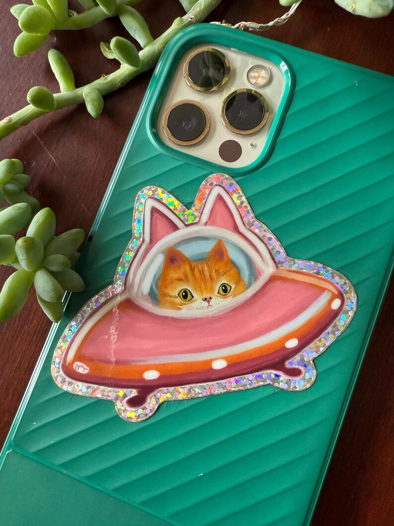 Cute and funny painterly orange kitty cat glitter sticker taking a spin in the abandoned pink alien flying saucer designed just for him-who wouldn’t?