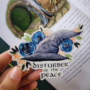 May include: A watercolor sticker of a wizard's hat with blue flowers and the text "Disturber of the Peace".