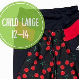 Könnte beinhalten: Schwarze Leggings mit rotem Kirschmuster und passendem Scrunchie. Die Leggings haben marineblaue Seiteneinsätze und rote Paspeln. Das Bild enthält den Text "CHILD LARGE 12-14".