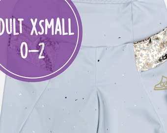 May include: Light blue leggings with a silver and gold foil design. The leggings have a pocket with a gold sequin design. A matching scrunchie and a tag that says "ADULT XSMALL 0-2" are also included.