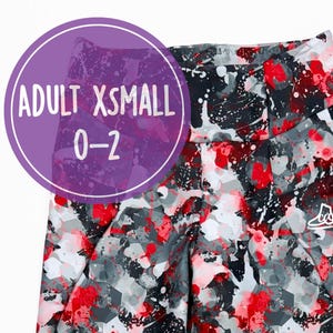 Könnte beinhalten: Leggings und passendes Scrunchie für Erwachsene XS/S. Die Leggings und das Scrunchie haben ein Design mit roter, weißer und grauer Spritzfarbe auf schwarzem Hintergrund. Die Leggings sind Größe 0-2.