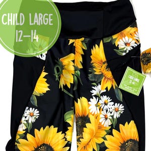 Könnte beinhalten: Schwarze Leggings mit einem Sonnenblumen- und Gänseblümchenmuster. Die Leggings haben schwarze Seitenteile und einen Bund. Die Leggings sind in Kindergröße L (12-14).