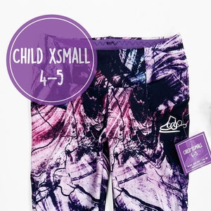 Könnte beinhalten: Lila, rosa und blaue Leggings mit abstraktem Muster und schwarzem Bund. Die Leggings sind mit "Child XSmall 4-5" gekennzeichnet.