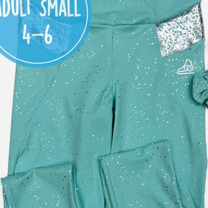 Könnte beinhalten: Türkisfarbene Leggings mit silbernen Glitzerakzenten und einem passenden Scrunchie. Die Leggings haben eine Tasche mit silbernen Pailletten und ein kleines Etikett mit der Aufschrift "ADULT SMALL 4-6".