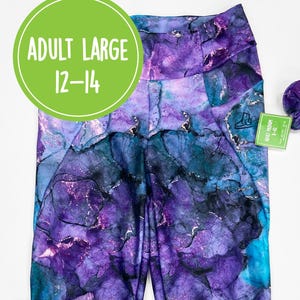 Könnte beinhalten: Hoch taillierte Leggings mit einem abstrakten Alkoholtintenmuster in Violett-, Blaugrün- und Schwarztönen mit metallischen Goldakzenten. Enthält ein passendes Haargummi. Ein grünes, rundes Etikett zeigt den Text ADULT LARGE 12-14.