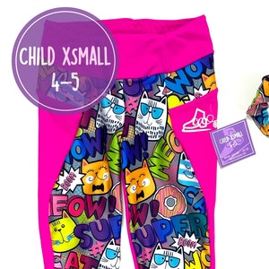Könnte beinhalten: Rosa und graue Leggings mit einem Katzen- und Comic-Druck. Die Leggings haben eine rosa Seitenleiste und eine Tasche am rechten Bein. Die Leggings sind für ein Kind in Größe 4-5. Ein graues und rosa Haargummi ist enthalten.