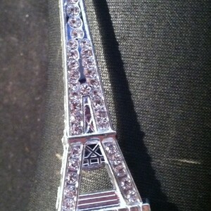 May include: A silver Eiffel Tower charm with rhinestones. The charm is a popular souvenir from Paris, France.