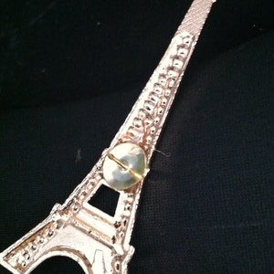 May include: A gold-colored Eiffel Tower ornament with a push pin attached to the back.