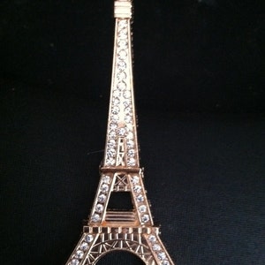 May include: A gold-colored Eiffel Tower keychain with a clear crystal design. The keychain is a small replica of the famous Parisian landmark.