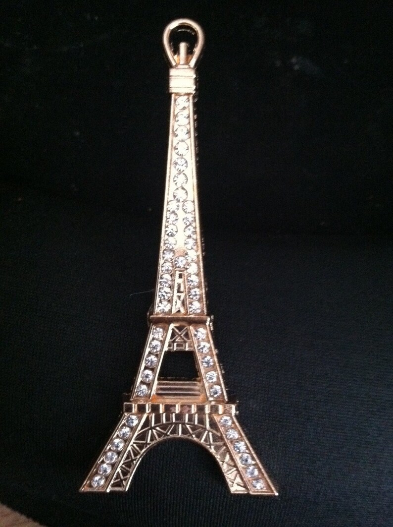 May include: A gold-colored Eiffel Tower keychain with a clear crystal design. The keychain is a small replica of the famous Parisian landmark.