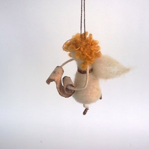 May include: A white felt angel ornament with a golden halo, holding a scroll in its hand. The angel has fluffy, golden hair and white wings.