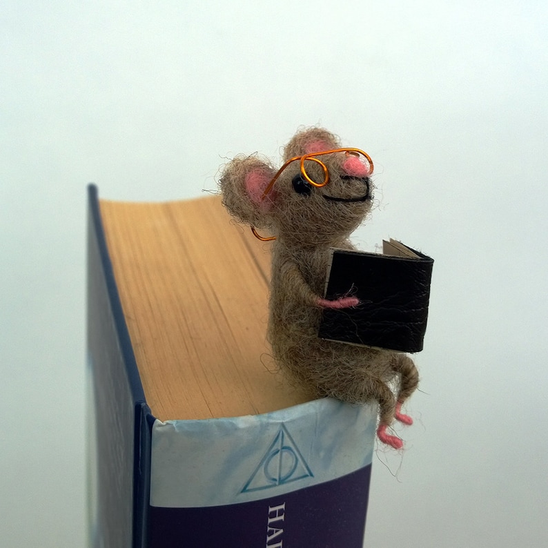 May include: A small gray felt mouse wearing orange glasses sits on a book with a black cover. The book has a blue and white cover with a triangle symbol and the word "Half" visible.